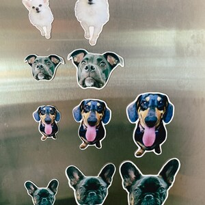 May include: A collection of dog breed magnets on a silver refrigerator. The magnets feature different dog breeds, including a chihuahua, a pit bull, a dachshund, and a french bulldog.