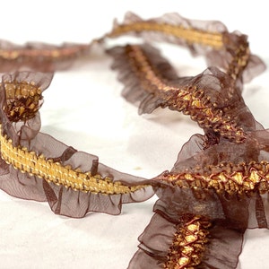 May include: Brown ruffled trim with gold metallic thread. The trim is made of a sheer fabric and has a delicate, feminine look.