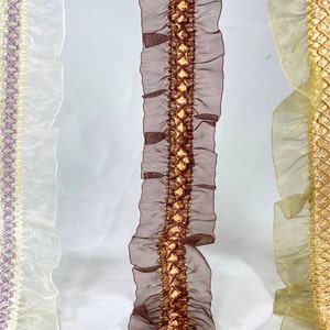 May include: Three different trims of ruffled fabric with a decorative braid down the center. The trims are in ivory, brown, and beige.