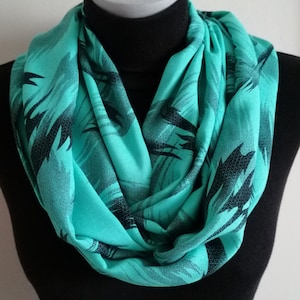 May include: A turquoise infinity scarf with a black abstract print. The scarf is made of a soft, lightweight fabric and is perfect for adding a pop of colour to any outfit.