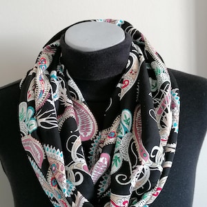 May include: A black infinity scarf with a paisley pattern in shades of pink, teal, and beige.