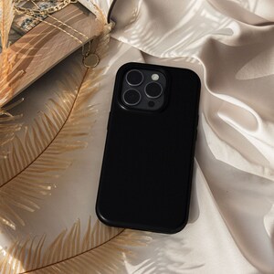 May include: A black phone case with a camera lens cutout. The case is lying on a beige fabric surface.