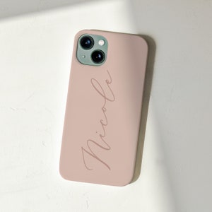 Puede incluir: Una funda de teléfono rosa claro con una lente de cámara blanca y el nombre "Nicole" escrito en cursiva.