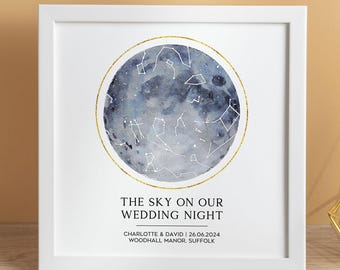 May include: A framed print showing a watercolour night sky with constellations, encircled by a gold ring. The text "THE SKY ON OUR WEDDING NIGHT" is below, along with names and a date. The print is in a white frame.