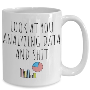 May include: White ceramic coffee mug with black text that reads "Look at you analyzing data and shit". The mug has a simple line graph and pie chart in color.