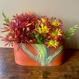May include: Orange ceramic vase with a cactus design, filled with a bouquet of red and yellow chrysanthemums.