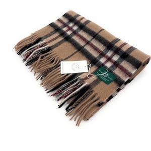 May include: A beige tartan scarf with black and claret-coloured checks. The scarf has a fringed edge and a tag attached. The scarf is made of a soft material, suitable for cold weather.