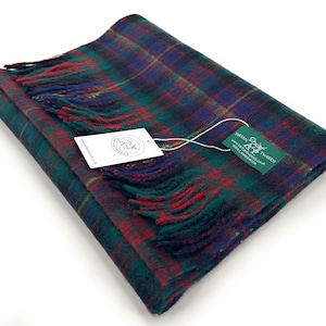 May include: A green, red, and blue plaid scarf with fringe. The scarf is folded in half and has a small green tag with the text "Tartan Tweeds" and a logo of a stag with antlers.