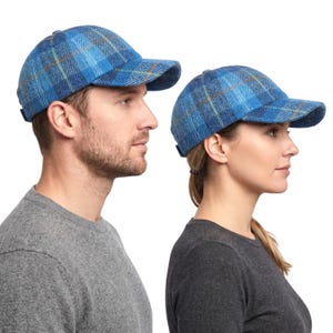 May include: Two blue plaid baseball caps. The caps feature a curved peak and an adjustable fabric strap. The plaid design incorporates blue, yellow, and brown hues. The caps are worn by two people.