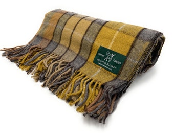 May include: A folded wool blanket with a plaid pattern in shades of yellow, gray, and brown. The blanket has a fringed edge and a green label that reads "Tartan Tweeds 100% Wool Blanket."