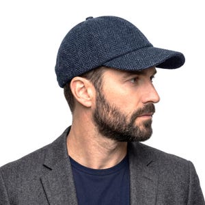 May include: A navy blue baseball cap with a herringbone pattern. The cap has a curved brim and a small button on top. The cap is made of a textured fabric and is a classic style.