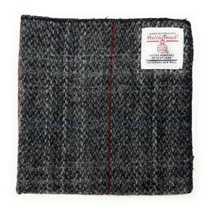Könnte beinhalten: Ein schwarzer und weißer Tweed-Stoffmuster mit einem roten Streifen in der Mitte. Der Stoff hat ein Etikett mit der Aufschrift "HAND WOVEN CLOTH Harris Tweed OUTER HEBRIDES OF SCOTLAND 100% PURE NEW WOOL".