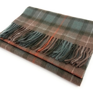 May include: A folded plaid scarf in shades of brown, green, and orange with a fringed edge. The scarf features a classic tartan pattern, perfect for adding warmth and style. The scarf is made of a soft material.