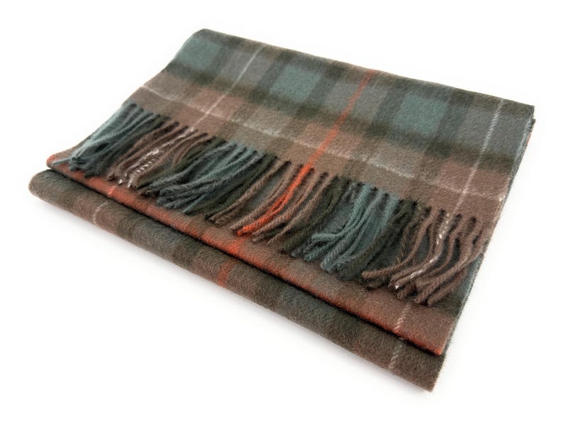 May include: A folded plaid scarf in shades of brown, green, and orange with a fringed edge. The scarf features a classic tartan pattern, perfect for adding warmth and style. The scarf is made of a soft material.