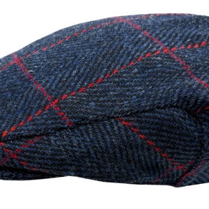 Puede incluir: Gorra plana de tweed azul marino con un patrón de cuadros rojos. La gorra está hecha de una tela texturizada y tiene una forma redondeada clásica. Un sombrero de estilo tradicional, adecuado para diversas ocasiones.
