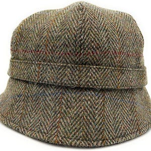 Peut inclure: Chapeau de type bucket en tweed vert, marron et bleu, avec un motif en chevrons. Le chapeau est orné d'une bande autour de la couronne et d'un bord légèrement incurvé. Le tissu est texturé.