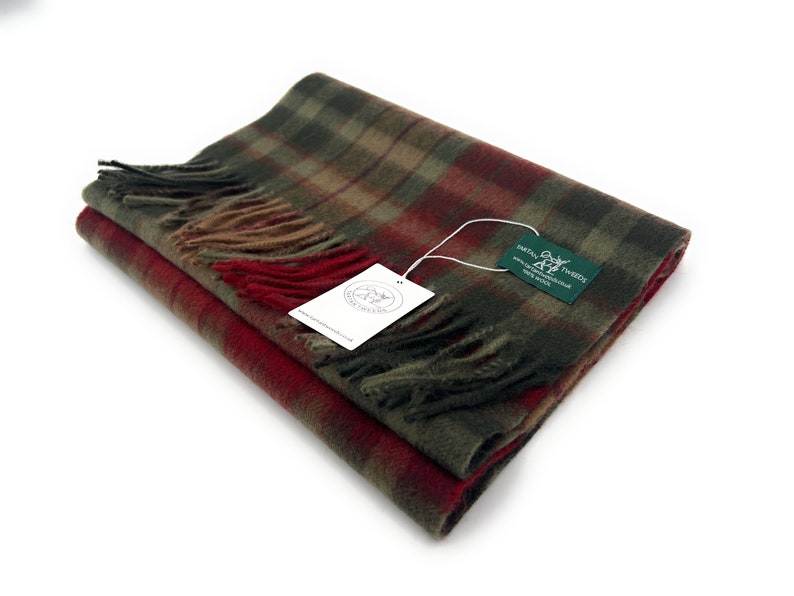 May include: A folded green, red, and brown plaid scarf with fringe. The scarf has a tag attached that reads "Harris Tweeds" and includes a website address.