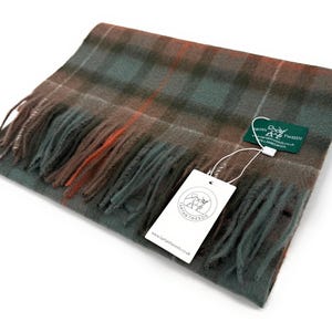 May include: A folded wool scarf in a plaid pattern with shades of green, brown, and orange. The scarf has fringed edges and a tag that reads "LANTAN TWEEDS". The scarf is a cozy accessory for cold weather.