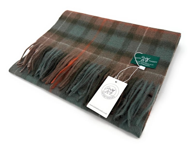 May include: A folded wool scarf in a plaid pattern with shades of green, brown, and orange. The scarf has fringed edges and a tag that reads "LANTAN TWEEDS". The scarf is a cozy accessory for cold weather.