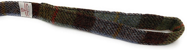 May include: A brown, blue, and green tweed strap with a white label that reads "Harris Tweed" and "Handwoven in the Outer Hebrides, Scotland".