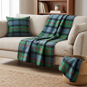 Peut inclure: Un coussin carré et une couverture rectangulaire présentant un motif à carreaux dans des tons de vert, bleu et noir avec de fines lignes rouges. La couverture est drapée sur un canapé et une pièce assortie est pliée dans un panier en osier.