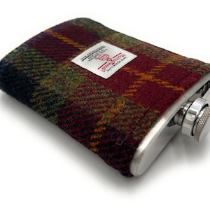 Könnte beinhalten: Eine Edelstahl-Taschenflasche mit einer roten, grünen und schwarzen karierten Stoffhülle. Die Hülle hat ein weißes Etikett mit dem Text "Original Penguin" und einem Globus-Logo.