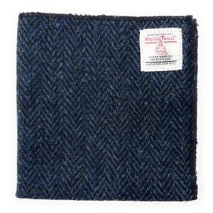 May include: A blue and black herringbone tweed fabric swatch with a white label that reads "HAND WOVEN CLOTH HARRIS TWEED OUTER HEBRIDES OF SCOTLAND 100% PURE NEW WOOL"
