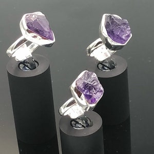May include: Three silver rings with amethyst gemstones. The rings are displayed on black stands.