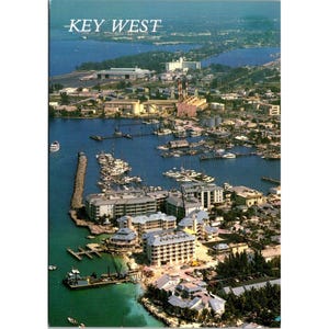 Puede incluir: Postal aérea de Key West, Florida. La imagen muestra un puerto lleno de barcos, rodeado de edificios y exuberante vegetación. El texto "KEY WEST" está impreso en la parte superior.