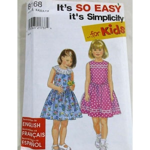 May include: A Simplicity sewing pattern envelope 8168 for kids sizes 3, 4, 5, 6, 7, 8. The front features illustrations of two dresses: one blue gingham with a floral print and a white collar, and one pink dress with white polka dots and trim.