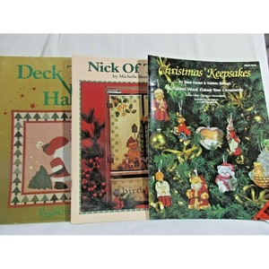 Könnte beinhalten: Drei Weihnachtsbastelbücher mit den Titeln "Deck the Halls", "Nick of Time" und "Christmas Keepsakes". Die Bücher zeigen Illustrationen von Weihnachtsornamenten, einem Vogelhaus und einem Weihnachtsmann.