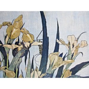 May include: A detailed print of irises in bloom. The artwork features yellow and cream-colored flowers with dark blue and green foliage against a light blue background. The style is reminiscent of traditional Japanese woodblock prints.
