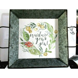 May include: A square metal tray with a green border and a white background. The tray has a floral design with a ladybug and the words "nurture your soul".