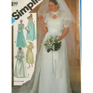Peut inclure: Une pochette de patron de couture Simplicity présentant une robe de mariée blanche avec un col haut, des manches courtes transparentes et une jupe longue. La couverture montre des illustrations de quatre variantes de robes, dont une robe de mariée avec voile.