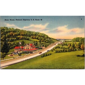 May include: Vintage postcard featuring a scenic view of the Stone House on National Highway U.S. Route 40. The image shows a long road winding through a valley, with a large building and flag on the left. Lush green fields and trees surround the road.
