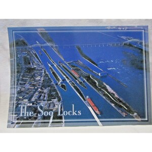 May include: An aerial view of the Soo Locks, with the text "The Soo Locks" at the bottom. The image shows the locks, waterways, and surrounding structures in shades of blue and green, with several ships.