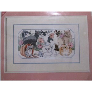 May include: Cross-stitch pattern depicting a group of nine cats in a garden setting. The cats are of various breeds and colours, including black, white, grey, orange, and tabby. The garden is filled with flowers and foliage.