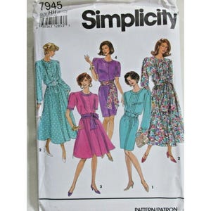 Puede incluir: Un sobre de patrón de costura Simplicity 7945 con ilustraciones de cuatro estilos de vestido diferentes. Los diseños incluyen un vestido de lunares, un vestido morado liso con fajín floral, un vestido rosa liso y un vestido con estampado floral.