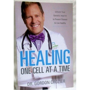 Può includere: Copertina di un libro con la foto di un uomo che indossa un camice bianco e un papillon viola. Il titolo del libro è "HEALING ONE CELL AT A TIME" e l'autore è "DR. GORDON CROZIER".
