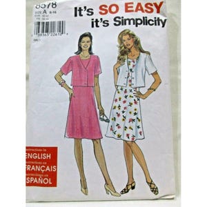 以下が含まれることがあります： 型紙ブランドSimplicityの8578番のパッケージ。2種類の服装のイラストが描かれている。一つは無地のピンクのワンピースと半袖ジャケットのセット、もう一つは花柄の白いワンピースと白い半袖ジャケットのセットである。