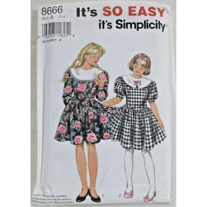 Puede incluir: Un sobre de patrón de costura Simplicity 8666 con dos diseños de vestidos. Un vestido tiene fondo negro con estampado floral rosa y azul y cuello blanco. El segundo vestido presenta un patrón de cuadros vichy en blanco y negro con cuello blanco.