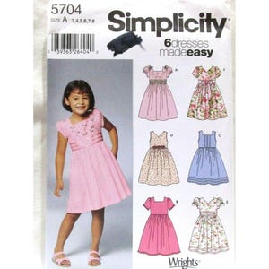 May include: A Simplicity sewing pattern envelope 5704 for six dresses in sizes 3, 4, 5, 6, 7, and 8. The front features a child wearing a pink dress and illustrations of six different dress styles, including floral and solid colour designs.