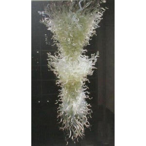 May include: A large, abstract glass chandelier with a cascading design. The fixture features multiple tiers of swirling, curly glass elements in shades of white and pale green. The overall shape is elongated and vertical, with a dark background.