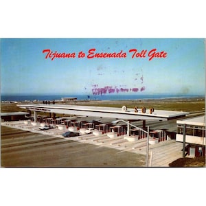 Puede incluir: Postal vintage que muestra un peaje con el texto "Tijuana to Ensenada Toll Gate" en rojo. La imagen muestra un largo toldo blanco con múltiples cabinas de peaje, coches y el océano al fondo. El cielo es azul claro.