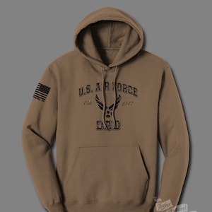 May include: A brown hooded sweatshirt with a black print of the U.S. Air Force logo and the text "U.S. AIR FORCE Est. 1947 DAD". The left sleeve has a small American flag patch.