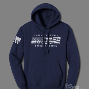 May include: Navy blue hooded sweatshirt with a white graphic of the word "Mustang" with an American flag design. The text "United States Navy" and "Sursum Corda" are also printed on the sweatshirt.