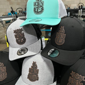 May include: A stack of five black, gray, and teal baseball caps with a brown leather patch featuring a stylized anchor and the text "USN" or "USN Retired".