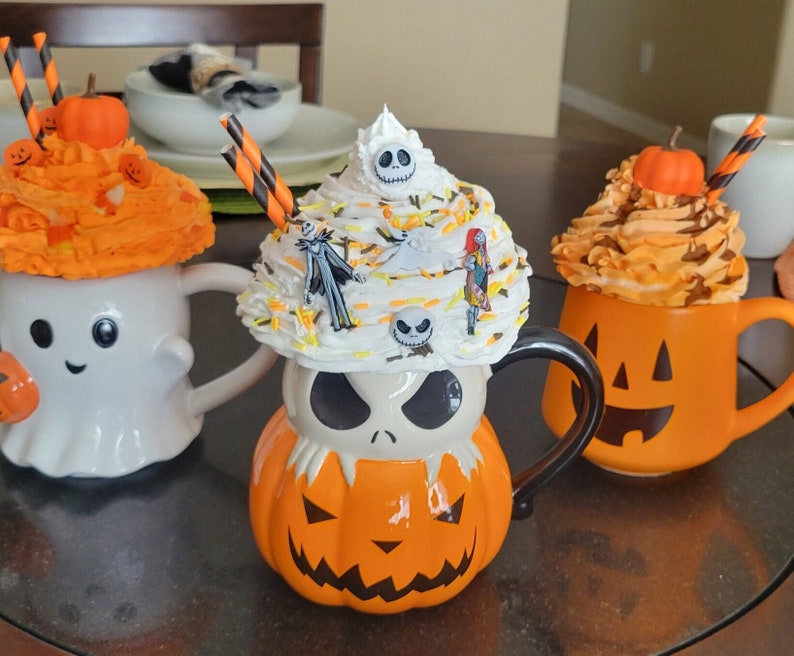 Puede incluir: Tres tazas con tem&aacute;tica de Halloween con coberturas decorativas de crema batida. Las tazas tienen forma de fantasma, calabaza y Jack Skellington. Cada taza tiene un dise&ntilde;o diferente y est&aacute; decorada con calabazas en miniatura y pajitas.