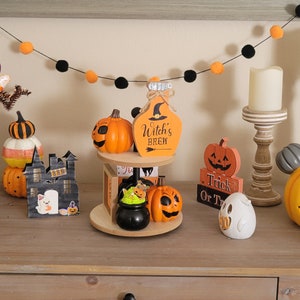 Puede incluir: Una colecci&oacute;n de decoraciones tem&aacute;ticas de Halloween, que incluyen figuras con forma de calabaza, una botella de poci&oacute;n de bruja y una calabaza de Mickey Mouse. La exhibici&oacute;n tambi&eacute;n presenta una guirnalda negra con pompones naranjas y negros y un &aacute;rbol decorativo con caramelos.