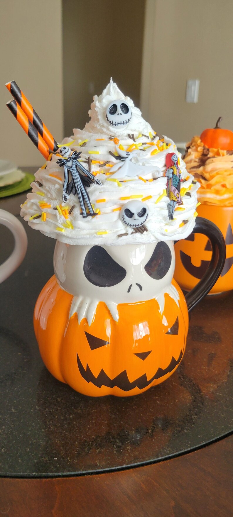 Puede incluir: Una taza tem&aacute;tica de Halloween con forma de calabaza con la cara de Jack Skellington. La taza est&aacute; cubierta con crema batida y figuritas de personajes. Incluye pajitas a rayas naranjas y negras.
